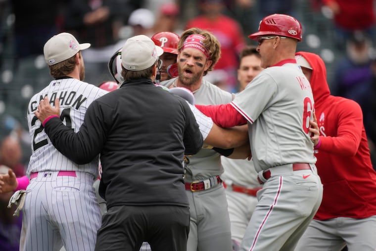 Philadelphia Phillies designated hitter Bryce Harper, back center, is held back from pursuing Colorado Rockies relief pitcher Jake Bird.