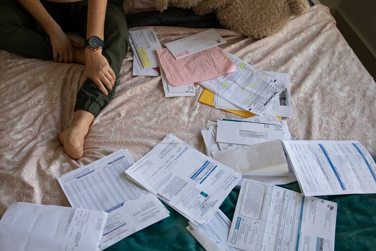Stephanie Sena sits on her bed surrounded by a folder full of medical bills from a foot amputation she had in 2019.