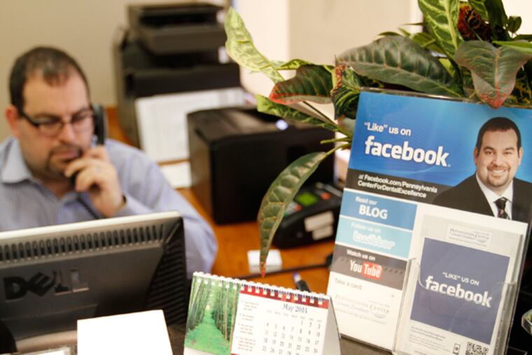 Dentist Leonard F. Tau talks with a patient on the phone about a Groupon deal. At right is a countertop display letting patients know he is on Facebook, Twitter, a blog, and Youtube. (MICHAEL S. WIRTZ/Staff Photographer)