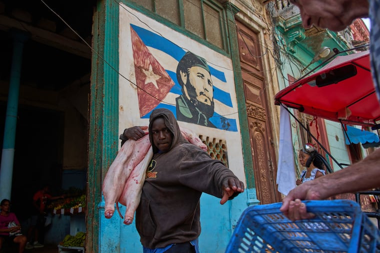 A man carries a pig at the entrance of a market, decorated with a mural of Fidel Castro, in Havana, Cuba, Wednesday, Aug. 12, 2026.