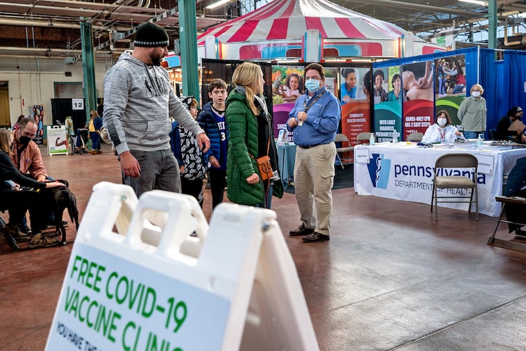 Tom McGroaty (center, wearing mask) with the Pennsylvania Department of Health, works like a carnival pitchman or barker, trying to attract attendees to the department’s COVID-19 vaccine pop-up clinic at the Pennsylvania Farm Show Jan. 10, 2022. The show returned to Harrisburg for its 106th year, after being virtual last year,