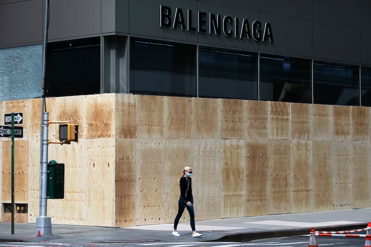 A woman walks by a boarded up Balenciaga store in June 2020 on Madison Avenue in New York. (AP Photo/Mark Lennihan)