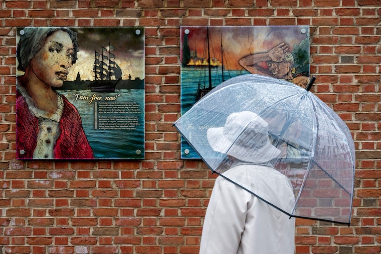 A visitor pauses at a panel about Ona Judge (left) at the President's House Site before community members, advocates, and leaders joined the Avenging The Ancestors Coalition (ATAC) for their annual gathering honoring Ona Judge’s life, resistance, and enduring impact.