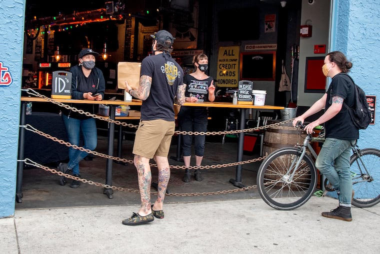 Bartender Rebecca Strapp (left) and manager Angelica Preso (right) talk to customers at the sidewalk walkup at Garage Passyunk on May 14 as they awaited passage of a cocktails-to-go bill.