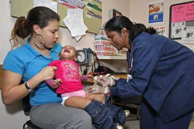 Hazelline Torres (left) holds her daughter Emery Torres as RN Saji Philip administers a shot at the city's District Health Center. ( Michael S. Wirtz / Staff Photographer )