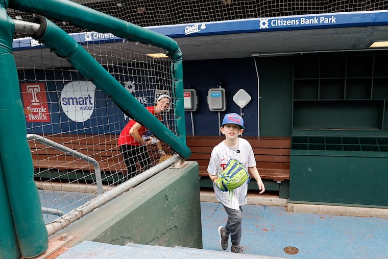 Lincoln Hanson walks from the Phillies' dugout with his mother, Megan Hanson, before the Phillies played the Kansas City Royals on Friday. Hanson, who has leukemia, enjoyed his time meeting with Phillies pitcher Matt Strahm and outfielder Brandon Marsh.