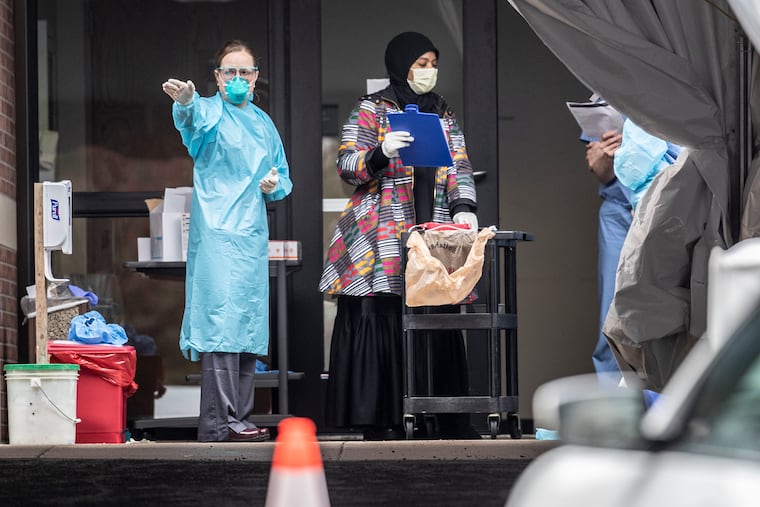 A physician Abington Hospital’s coronavirus testing tent indicates which vehicle they need to visit next with the tray containing the test kit on Tuesday.