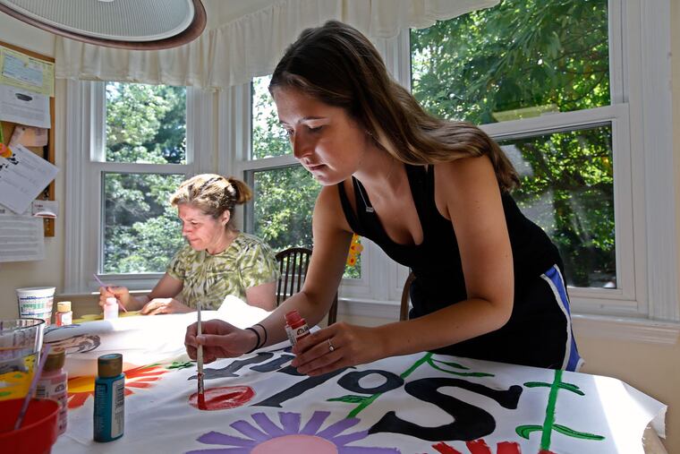 Devon Braunstein (right) paints a red flower banner that will be carried during the “Clean Energy March” from Philadelphia City Hall to Independence Mall. Her group is part of the “Solutions Brigade” during the march.
