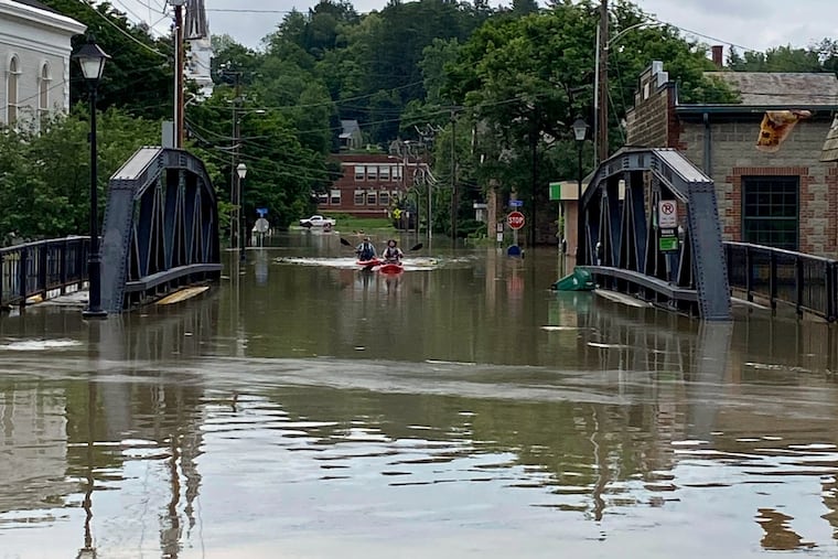 Two kayakers paddle through floodwaters as they approach the School Street Bridge in Montpelier, Vt.