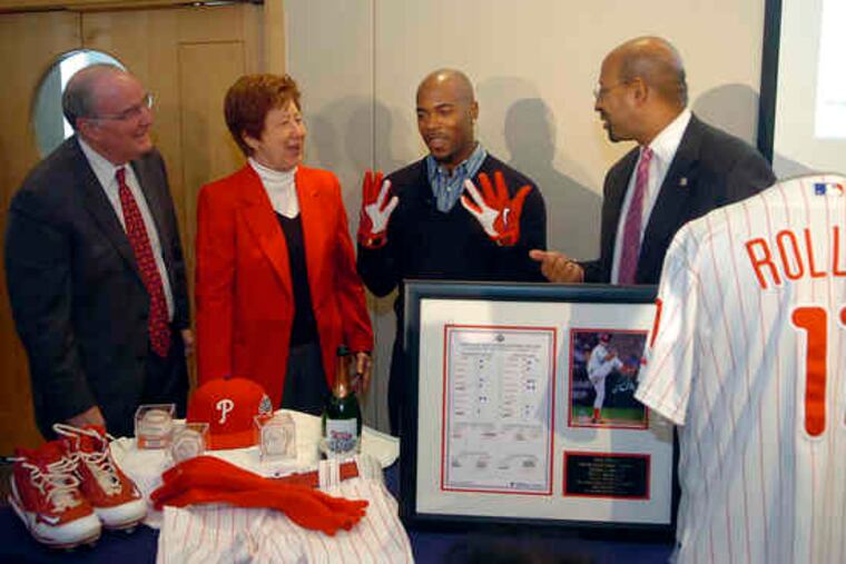 PHILLIES shortstop Jimmy Rollins (in gloves) is joined by team president David Montgomery (left) in presenting Rollins' 2008 championship-season uniform and other team memorabilia to the Atwater Kent Museum during a news conference yesterday at the Independence Visitors Center. Accepting the donations were Mayor Nutter and museum CEO Viki Sand.
