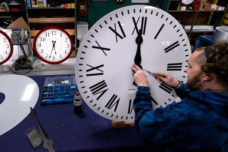 Ian Roders fastens the hands of a clock at the Electric Time Company in Medfield, Mass. in November 2022.