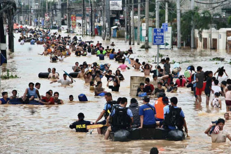People wading in the floodwater in suburban Cainta, east of Manila. Rescuers yesterday plucked bodies from muddy floodwaters and scrambled to reach survivors on rooftops.