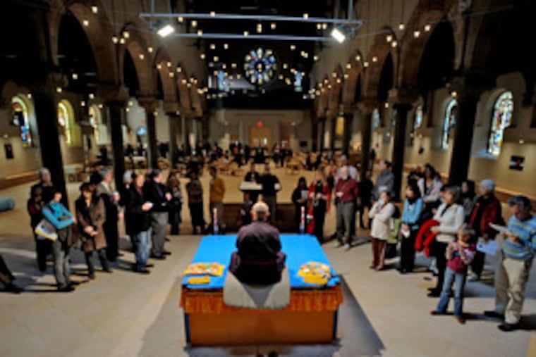 Losang Samten sits atop a platform in the Philadelphia Cathedral, where onlookers watch him begin work on the mandala. The Buddhist ritual portrays a message of life.