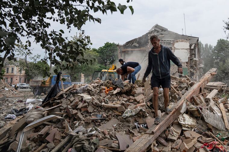 Local residents search for documents of their injured friend in the debris of a destroyed apartment house after Russian shelling in a residential area in Chuhuiv, Kharkiv region, Ukraine, Saturday, July 16, 2022.