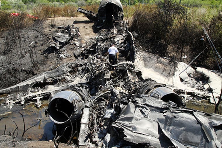 A National Transportation Safety Board official looks through the wreckage at the scene Monday, June 2, 2014, in Bedford, Mass., where a plane plunged down an embankment and erupted in flames during a takeoff attempt at Hanscom Field Saturday, May 31, 2014. Lewis Katz, co-owner of the Philadelphia Inquirer and six other people died in the crash. (AP Photo/Boston Herald, Mark Garfinkel, Pool)