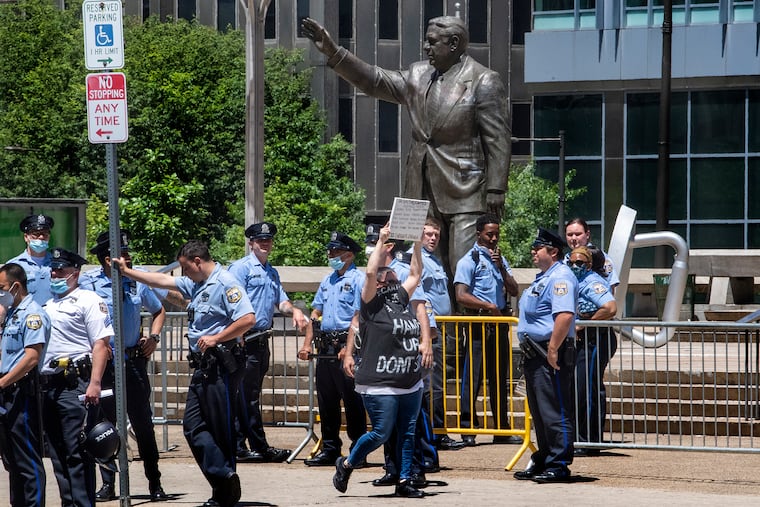 A protester walks near the Frank Rizzo statue as Philadelphia police guards the are during a protest in 2020.