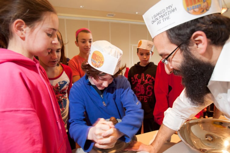 Rabbi Shaya Deitsch (right) helps Daniel Hoffman, 12, and other children grind wheat for matzo at the Chabad Jewish Education Center in Fort Washington. (Ed Hille / Staff Photographer)