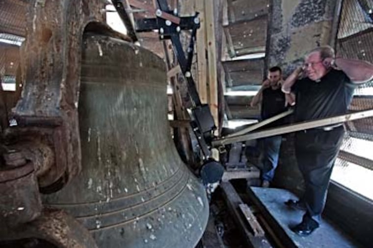 In the clock tower of St. John the Baptist Church in Manayunk, the Rev. James A. Lyons (right) and maintenance worker John Woods react as the bell chimes 3 p.m. A neighbor complained to the city about the 7 a.m. peal. (DAVID M WARREN / Staff Photographer)