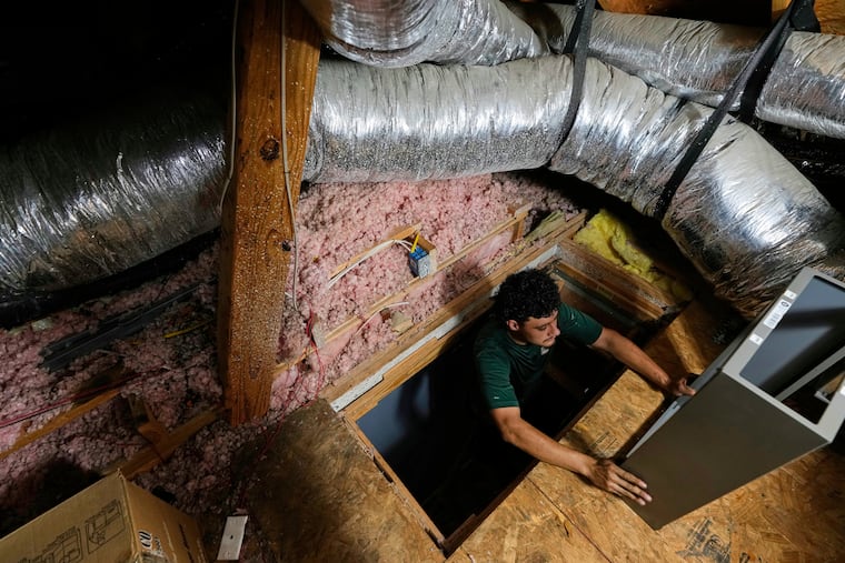 An installer climbs into an attic with parts of a new HVAC system that was installed in a residential home in Fate, Texas, in 2025.
