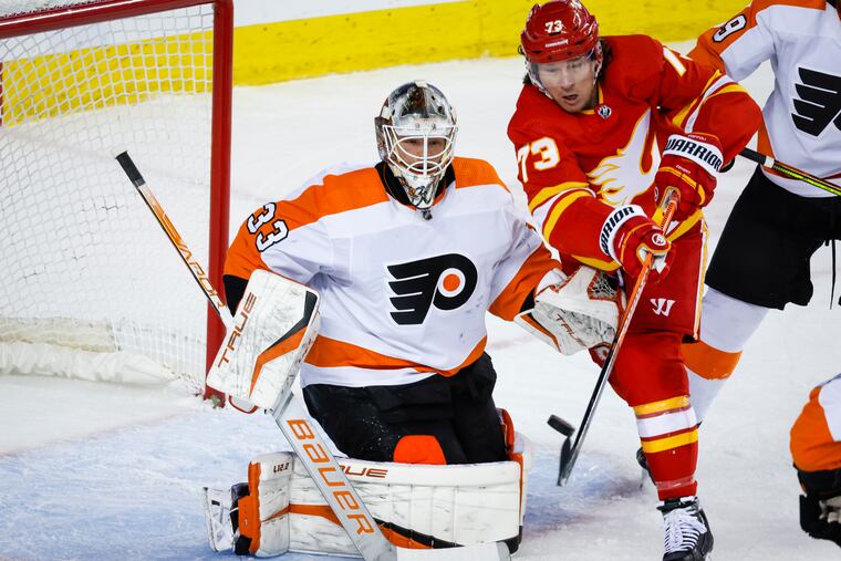 Philadelphia Flyers goalie Samuel Ersson, left, looks on as Calgary Flames forward Tyler Toffoli tries to deflect the puck into the net during the first period of an NHL hockey game in Calgary, Alberta, Monday, Feb. 20, 2023. (Jeff McIntosh/The Canadian Press via AP)