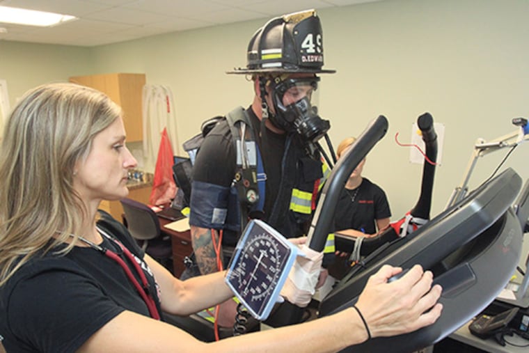 Deborah Feairheller, left, has a Ph.D.in exercise physiology and sports science and teaches at Ursinus College. The Penn State grad and mother of three also is a volunteer firefighter. She performs a test on Dane Edwards, 23, a firefighter in full uniform, walking on a treadmill.