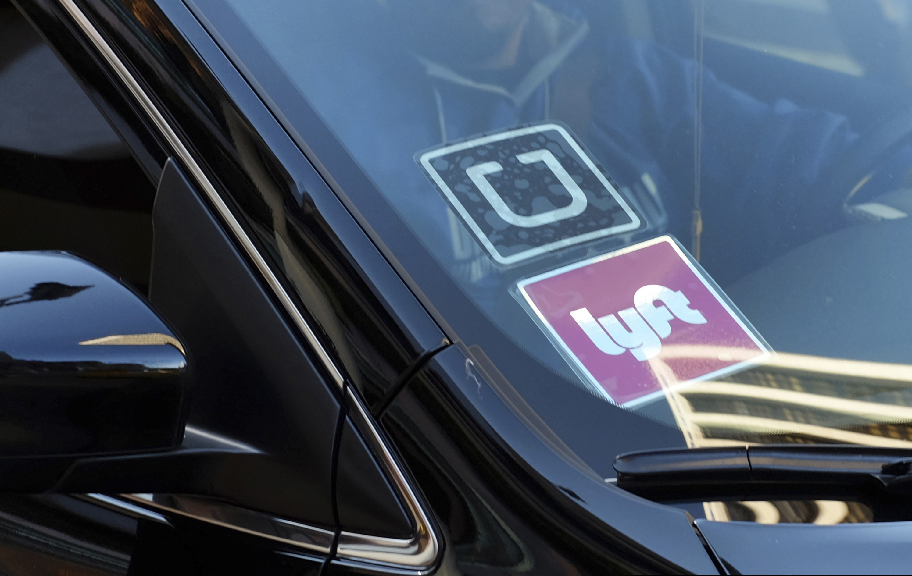 FILE - In this Jan. 12, 2016, file photo, a ride-share car displays Lyft and Uber stickers on its front windshield in downtown Los Angeles. Law enforcement agencies and ride-hailing companies are intensifying efforts to warn passengers against getting in without checking to ensure both the vehicle and driver are legitimate.