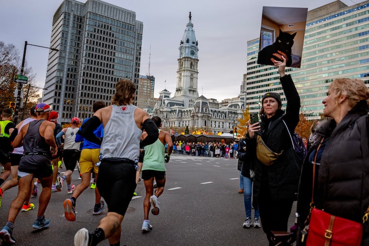 Tracking him on her phone app, Angela Pietschmann watches for her husband, Geoffrey Gund, while holding a photo of their pet cat, Miles, at the start of the 2024 Philadelphia Marathon in Sunday, Nov. 24, 2024. Her mom, Jeanette Pietschmann, is at right.