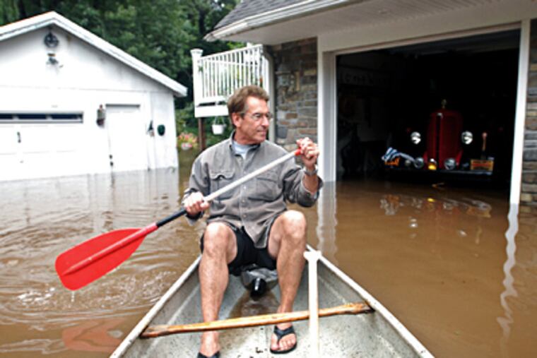 Brad Varney paddles a canoe around his home as floodwaters from the Delaware River slowly recede on Morgan Avenue in Yardley. (Matt Stanley / Bucks County Courier Times)
