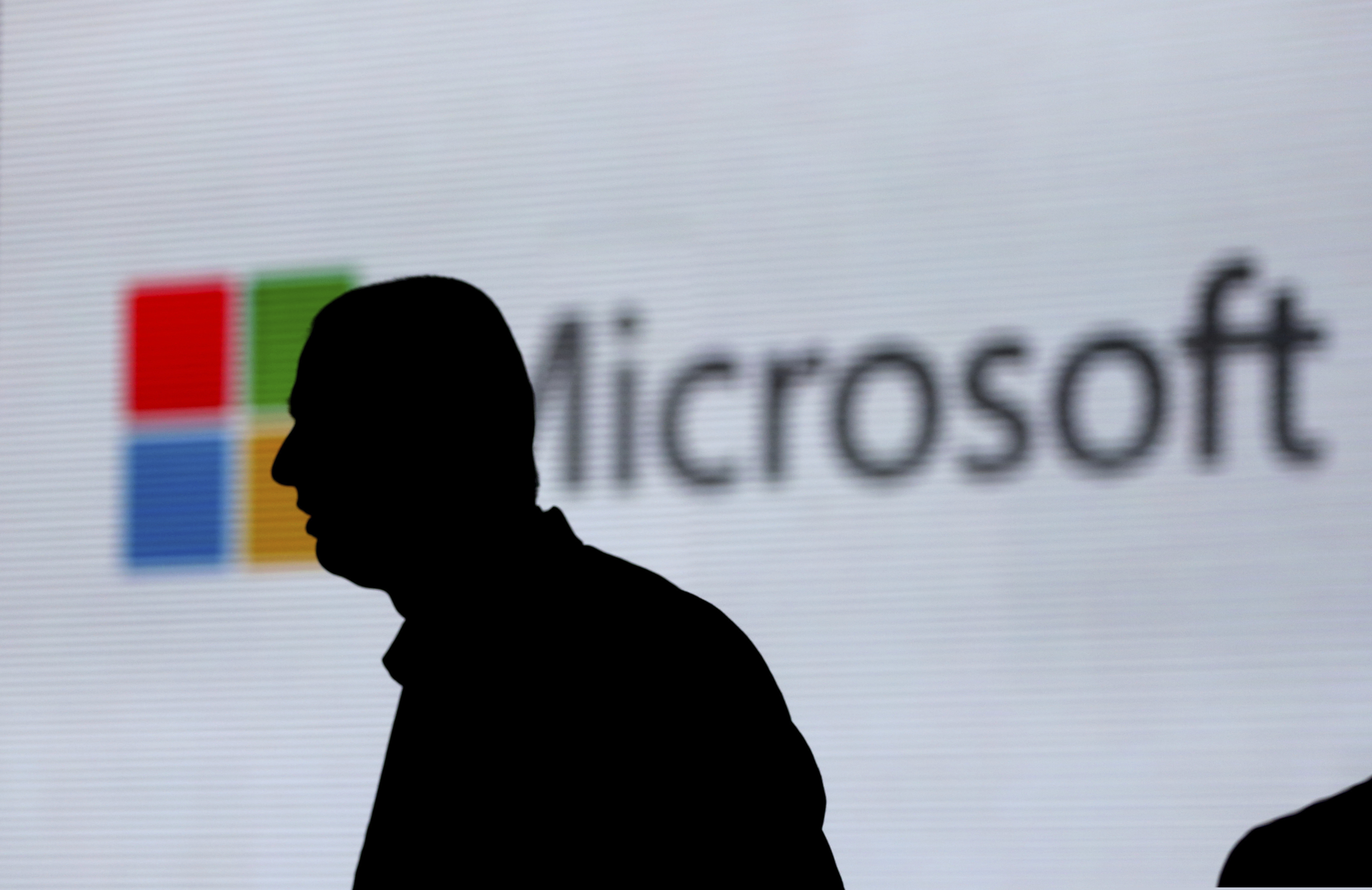 In this Nov. 7, 2017, file photo, an unidentified man is silhouetted as he walks in front of Microsoft logo at an event in New Delhi, India. Microsoft is in a fierce popularity contest with upstart work messaging service Slack. Both are widely used by small businesses. (AP Photo/Altaf Qadri, File)