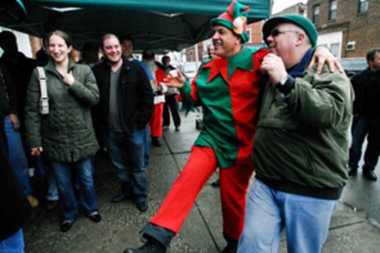 Ray the Elf dances with Vinny Roth outside Isgro Pastries. This year, Ray Verbrugghe and Tony Ciaccio Sr. led a band of 20 merry men on a bus trip from the suburbs into the Italian Market for the soggy pre-Christmas revelry.
