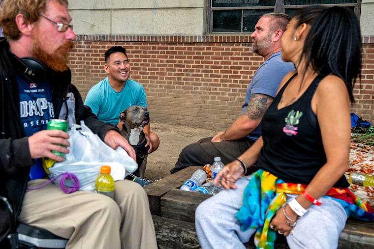Executive director Luke Stivala (center) is with Rellik the pit bull as he talks with clients outside Breaking Bread Community Shelter in Upper Darby in July. The shelter is closed during the day, and its twice-daily food service was eliminated after Delaware County cut funding for its homeless shelters.