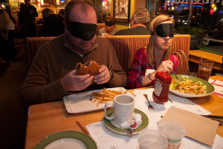 From left, Craig Westphal and Jenny Westphal wear eye masks to experience what it is like to eat food without sight Monday at Applebee's.