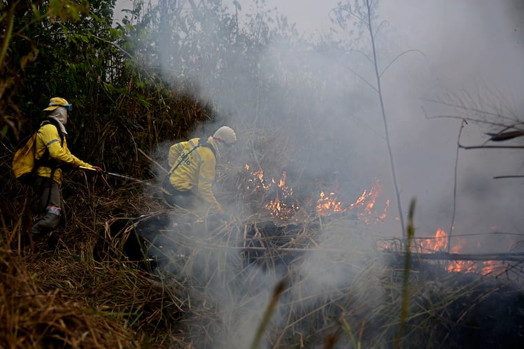 Firefighters work to put out fires along the road to Jacunda National Forest, near the city of Porto Velho in the Vila Nova Samuel region which is part of Brazil's Amazon, Monday, Aug. 26, 2019. The Group of Seven nations on Monday pledged tens of millions of dollars to help Amazon countries fight raging wildfires, even as Brazilian President Jair Bolsonaro accused rich countries of treating the region like a "colony."