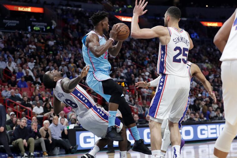 Heat swingman Jimmy Butler (22) looks to pass as Sixers shooting guard Shake Milton (18) and point guard Ben Simmons (25) defend.