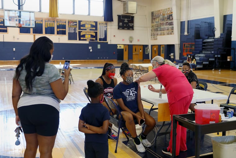 Nurse Kimball Dunlap (in pink) administers the first dose of the Pfizer COVID-19 vaccine to Allana Gray, 16, as her siblings Jason Collins (right), 13, and Jazmyne Collins (rear), 16, wait their turns during a vaccination clinic at Cheltenham High School in May.