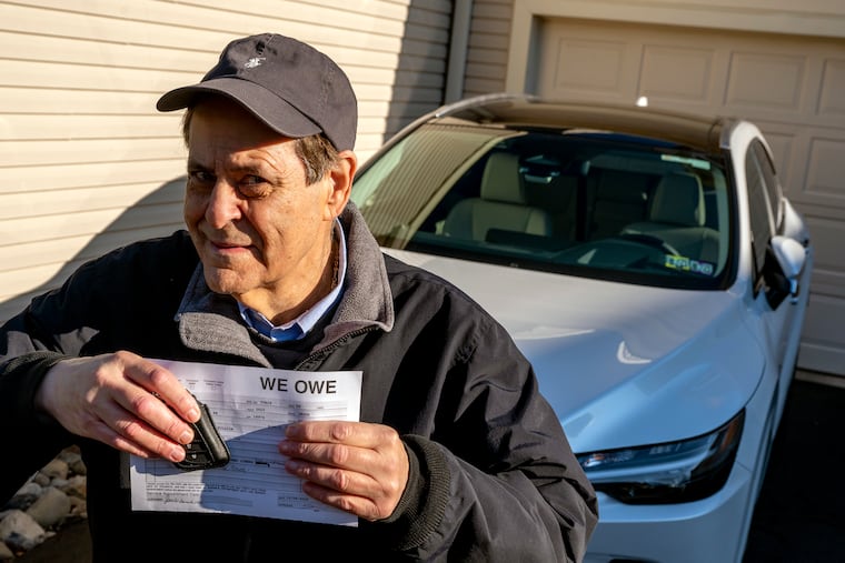 Joel Mickelberg poses with his brand new Lexus - and his “We Owe You” note and single key fob - outside his Warminster home Monday Jan. 9, 2023. Cars are being delivered to dealerships with pieces missing because of supply chain issues. Mickelberg only got one key fob - and no upgraded floor mats - with his new car.