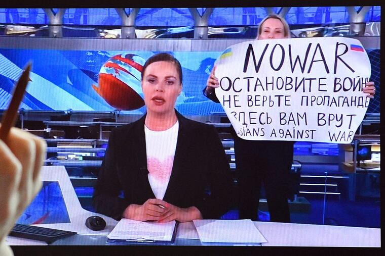 As news anchor Yekaterina Andreyeva, center, discusses Russia's relations with Belarus, Marina Ovsyannikova, right, burst into view, holding up a handwritten poster saying "No war" in English.