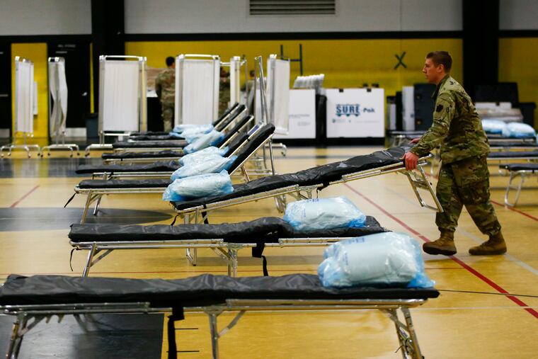 A member of the 103rd Brigade Engineer Battalion National Guard adjust a cot bed in the gymnasium at the Glen Mills School. FEMA and National Guard members will assemble medical equipment and beds in the field hospital to make room for coronavirus patients elsewhere.