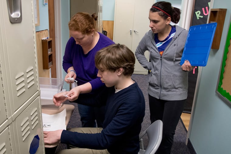 Gavin Moynagh, 16, does some work at Timothy School in Berwyn under the guidance of teaching assistant Chrissy Neely (left) and teacher Gianna Cappelli during school on Dec. 21.
