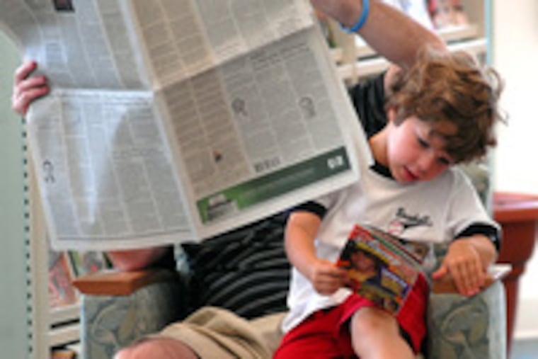 Sam Malloy, 4, of West Chester, gets in some serious reading while father Terry takes a look into the Wall Street Journal at the Avalon Free Public Library.
