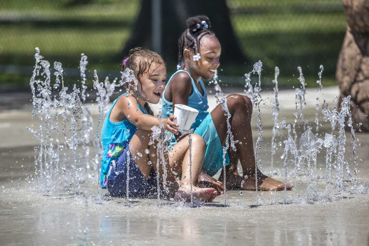 Natalie Roman (left), 7, and Arianna Clark, 8, sit in the middle of a water spray circle that sprays up from the ground Thursday afternoon in Camden.