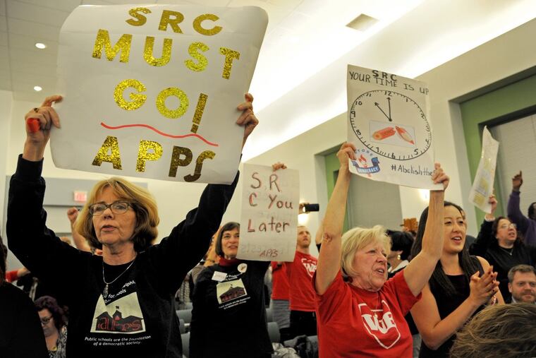 Retired Phila. school teachers Lisa Haver (left) and Diane Payne (right) hold their signs after the School Reform Commission takes its historic vote to dissolve itself.