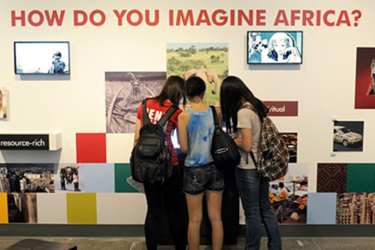 Visitors gather at a touchscreen video terminal that is part of the exhibit. Video screens intermixed with photos show images of Africa selected by visitors, who can change the video content using the terminal.