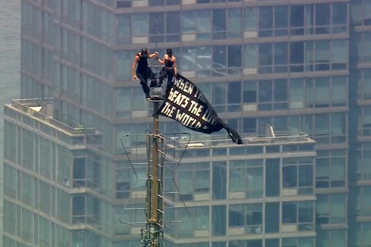 Two people stand on the tip of the antenna of the Empire State Building in New York while holding a banner on Wednesday, July 1, 2026.