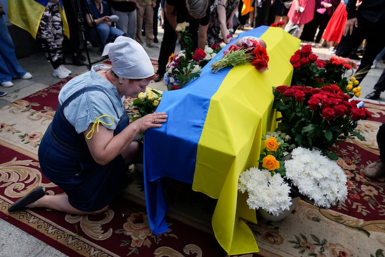 A woman kneels at activist and soldier Roman Ratushnyi's coffin during his memorial service in Kyiv, Ukraine.