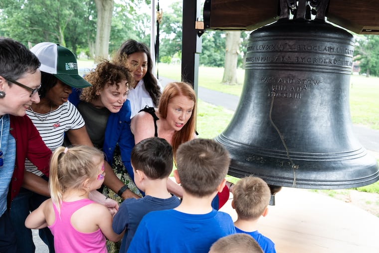 Sue Slawson (center left), commissioner of Philadelphia Parks & Recreation, and Jane Golden (center right), founder of Mural Arts, ring a replica of the Liberty Bell with other organizers and young attendees at the WaWa Welcome America media preview for the Philly Fair 250, outside the Please Touch Museum in West Philadelphia, on Thursday, June 18, 2026