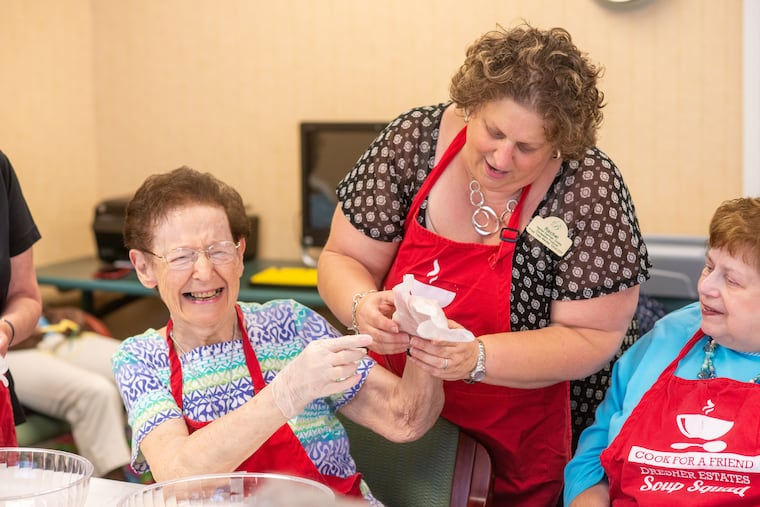 Rachel Kaufman Schatz (middle) helps Evelyn Schwedock, 87, (left) put on her gloves as the Soup Squad at Brandywine Living at Dresher Estates prepares to make vegetable soup. Once a month, the residents get together to make soup for seniors who need food while living at home. Suzi Kaufman, 81, right, was one of the group's original members.