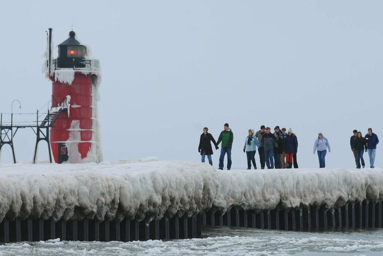 Pedestrians step along an ice-covered pier in South Haven, Mich. In Holland, Mich., a driver lost control of his car on an icy street and slammed into a hotel wall, injuring a woman inside.