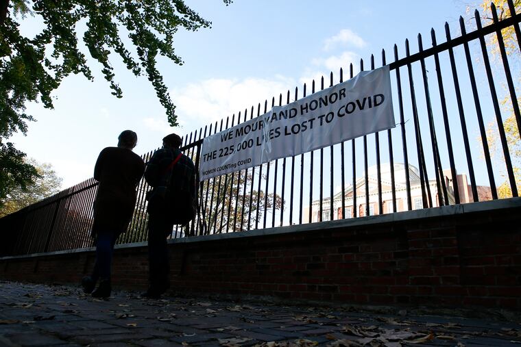 A couple on Saturday walks past a sign on a fence at the Pennsylvania Hospital mourning those who have lost their lives to the COVID-19 virus.
