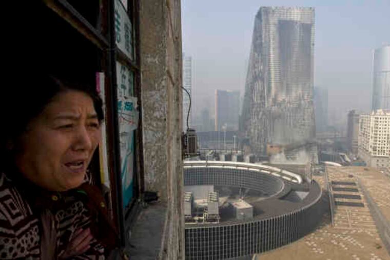 A woman looks out from her apartment near the Mandarin Oriental hotel, at right, which was destroyed. Beijing's propaganda ministry clamped a lid on news reports on the fire.